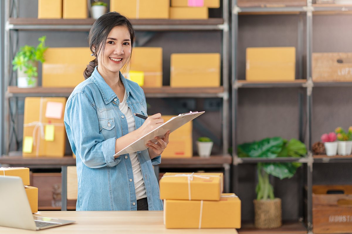 A small business owner is holding a clipboard and pen, smiling at the camera.