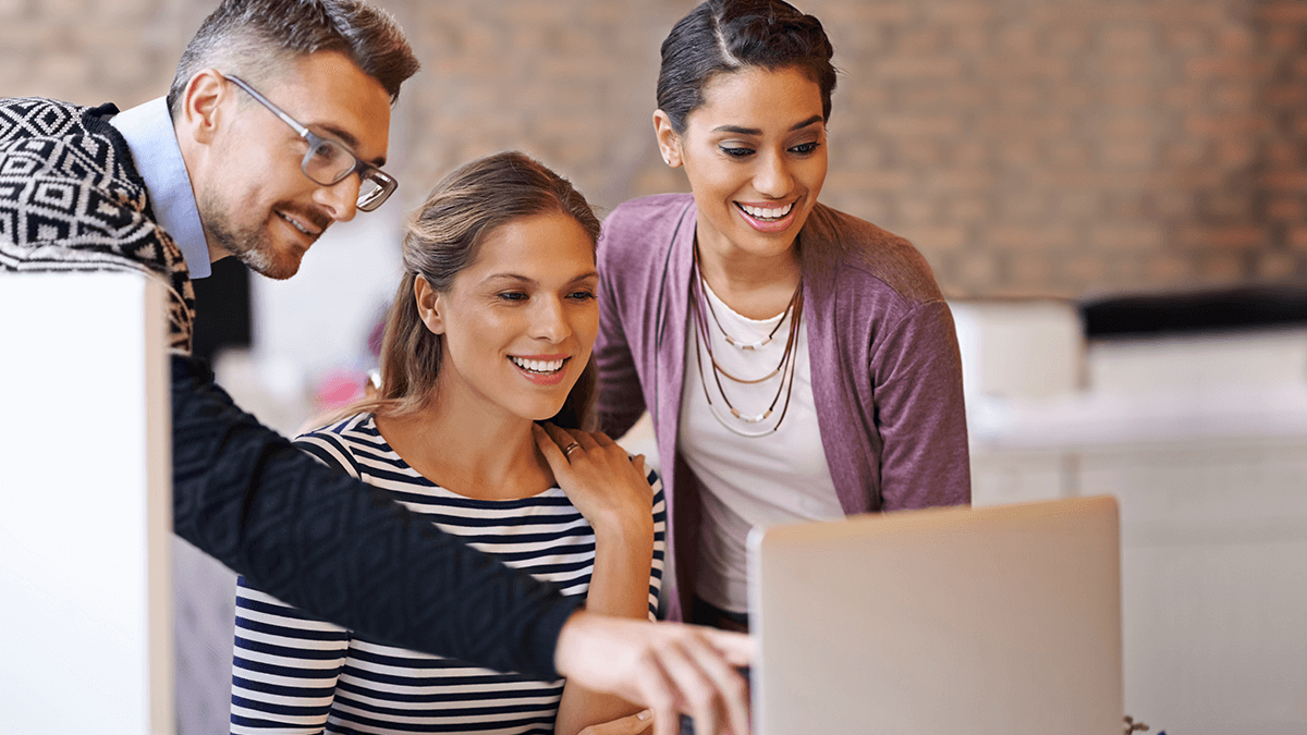 Man pointing at computer screen with two women standing next to him.